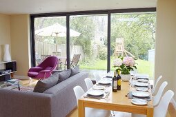 Set dining table, white classic shell chairs, lounge area and glass wall with garden view
