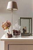 Glass jar full of conkers, table lamp, vase of hydrangeas and wooden sculptures in glass display case