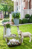 Basket of eggs, lamb statue and flowers in metal containers on rustic wooden table in garden