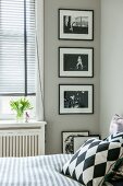 Blick über Bett mit Kissen auf schwarz-weiße Fotos an hellgrauer Wand neben Fenster