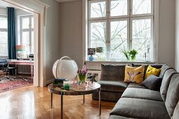 Corner sofa and round coffee table on herringbone parquet floor in pale grey living room