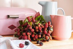 Bouquet of blackberries amongst jugs and bread bin in pastel shades