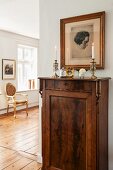 Portrait above candlesticks on cabinet and Baroque chair in background on wooden floor