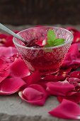 Rosengelee mit Zitronenmelisse in Glasschälchen auf Rosenblütenblätter