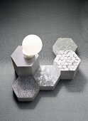 Fabric patterns on honeycomb-shaped objects in shades of grey and an opal glass lamp