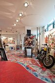 Artist's studio in loft with colourful pictures on wall, brightly painted floor and motorbike at the front right