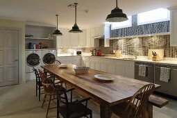 Long wooden dining table and various chairs in front of fitted kitchen in basement