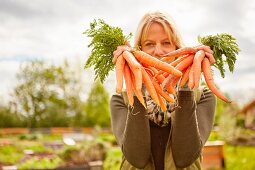 A woman in a garden holding bunches of freshly harvested carrots