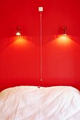 Bed below spotlights on bright red wall