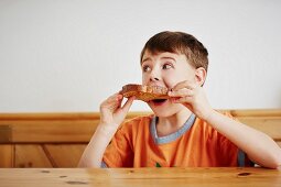 A boy sitting at a table biting into a slice of bread