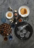 Bowl of nuts, crystal glasses on black tray and glass lampshade on concrete surface