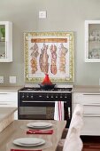 Painted and framed wall tiles as splashback behind gas cooker; place settings on counter in foreground