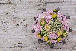 Blumengesteck aus Chrysanthemen und Schafgarbe auf rustikaler Holzunterlage