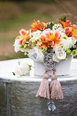 Festliches Blumengesteck mit Silberschmuck und Quasten auf versilbertem Tisch