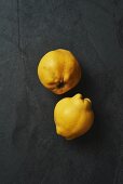 Two fresh quinces on a grey surface (seen from above)
