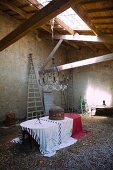 Table with tablecloths below chandelier suspended from wooden ceiling with skylight in old barn