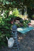 Watering can hanging on old bottle rack next to garden table on gravel floor