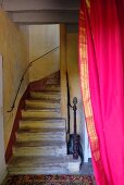 Vintage Treppenhaus mit gemauerter, gewendelter Treppe, an Wand filigraner Handlauf, seitlich im Vordergrund pinkroter Vorhang