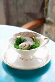 Easter arrangement of quail egg, moss and feather in coffee cup