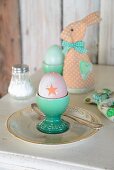 Boiled egg in turquoise eggcup in front of textile rabbit-shaped egg warmers