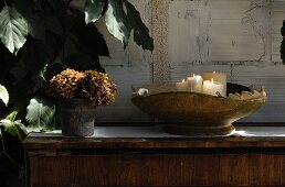 White candles in vintage bowl and pot of dried flowers