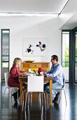 Man and woman at wooden breakfast table on modern white chairs in contemporary interior