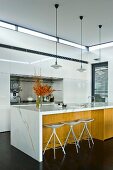 Kitchen island with white worksurface and wooden fronts, bar stools and classic pendant lamps