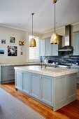 Island counter with marble worksurface and blue base units below brass pendant lamps in country-house kitchen