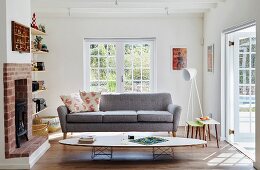Klassiker-Couchtisch vor grauer Couch in Wohnzimmer mit offenem Kamin