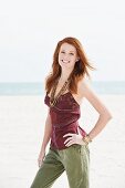 A young woman on a beach wearing a spaghetti strap top and cotton trousers