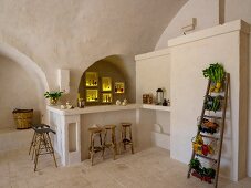 Illuminated niches above masonry counter and bar stools next to baskets of vegetables on ladder shelves
