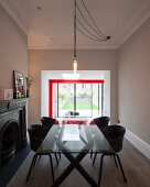 Hängeleuchte mit Glühbirnen über Glastisch mit schwarzen Schalenstühlen in modernisiertem Wohnraum, im Hintergrund breiter Durchgang und Blick auf rote Stahlkonstruktion