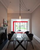 Light-bulb pendant lamp above glass table and black shell chairs in modernised interior with red steel structure seen through wide, open doorway in background