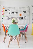 Table and colourful shell chairs in front of decorations hung on perforated wall panel