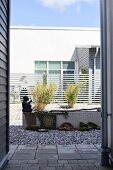 Blick auf betonierten Wasserlauf mit Skulptur in Patio mit Kiesboden und Bambussträuchern