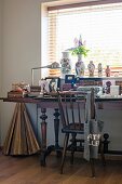 Antique wooden chair at cluttered desk with turned legs below window with vases on sill