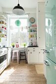 Küche mit rustikalem Dielenboden, hellblauem Kühlschrank, Barhockern am Fenster und offenen Wandregalen