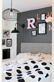Double bed with upholstered headboard and black and white polka-dot bed linen below decorative letters on dark grey wall