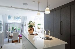 Glossy white island counter and dark brown fitted cupboards in elegant, open-plan kitchen