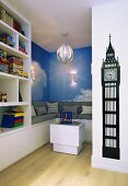 Play area with integrated bench, photo mural of clouds and collection of toys on white shelves; black wall sticker of Big Ben clock tower in foreground