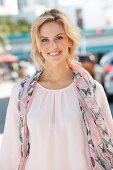 A young blonde woman wearing a light pink shirt with a silk scarf