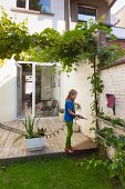 Girl watering plants growing in guttering mounted on garden wall