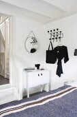 View across grey blanket on bed to white cabinet next to doorway with wooden steps and classic black Hang-It-All coat rack