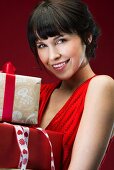 Dark-haired woman wearing red sleeveless dress holding wrapped gifts