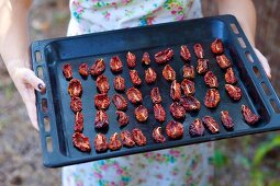 A woman holding a baking tray of dried tomatoes