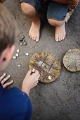 Noughts and crosses game played by children using pebbles and game board on disc of wood