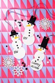 Weihnachtliche DIY-Geschenkanhänger mit Schneemann-Motiv auf Geschenkpapier mit geometrischem Muster