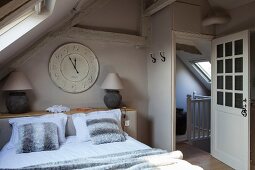 Dachgeschoss-Schlafzimmer mit Doppelbett und Vintage-Uhr, seitlich offene Tür mit Blick ins Treppenhaus