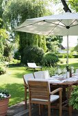 Gedeckter Tisch unter Sonnenschirm in gepflegtem Garten