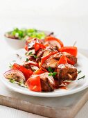 Barbecued meat skewers with red onions, peppers and herbs